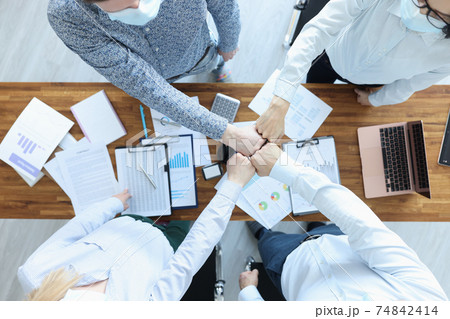 Group of business people sitting at table and touching their fists tip view Group of business people sitting at table and touching their fists tip view 74842414