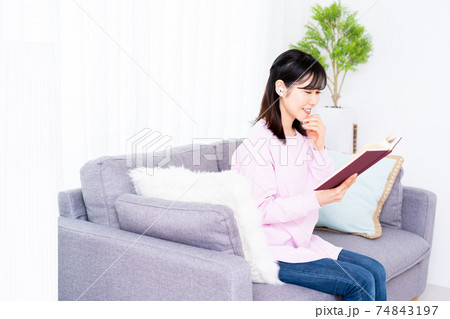 ソファーで音楽を聴きながら読書をする若い女性 ソファーで音楽を聴きながら読書をする若い女性 74843197