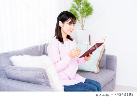 ソファーで音楽を聴きながら読書をする若い女性 ソファーで音楽を聴きながら読書をする若い女性 74843198