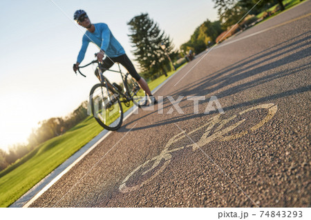 Close up of a bicycle sign drawn on asphalt. Professional male cyclist standing with his bike on a cycle path in the background 74843293
