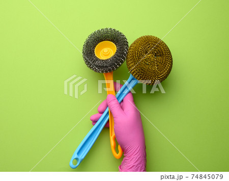 female hand in purple rubber gloves holds a plastic cleaning brush on green background female hand in purple rubber gloves holds a plastic cleaning brush on green background 74845079