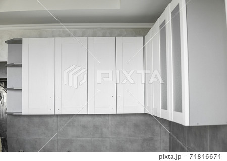 Custom kitchen cabinets installation with a white furniture facades mdf. Gray modular kitchen from chipboard material on a various stages of installation. A frame furniture fronts mdf profile. 74846674