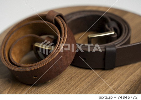 Two brown leather men's belts with bronze clasp on wooden chair with a white background. Handmade leather belt. 74846775