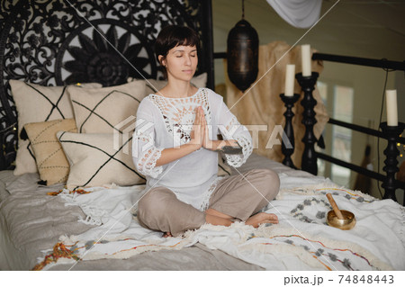 Young beautiful woman practicing yoga sitting in Namaste pose on bed. 74848443
