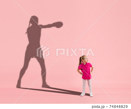 Childhood and dream about big and famous future. Conceptual image with girl and shadow of fit female boxer on coral pink background 74848829