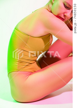 Tired female gymnast sitting on floor in studio Tired female gymnast sitting on floor in studio 74850150
