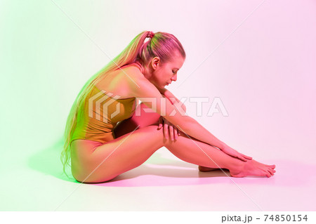 Tired female gymnast sitting on floor in studio Tired female gymnast sitting on floor in studio 74850154