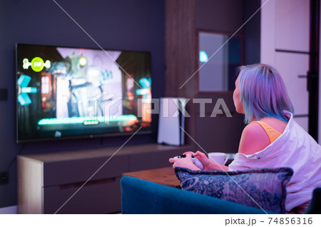 Beautiful blue haired girl holding gaming contorller playing video games at home. Back view. Beautiful blue haired girl holding gaming contorller playing video games at home. Back view. 74856316