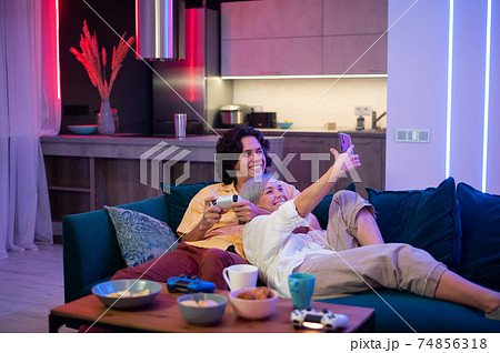 Happy young couple playing and winning a game funny activity sitting home on a sofa 74856318