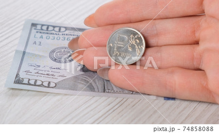 a female hand holds a Russian one ruble coin over a hundred dollar bill. Currency rate concept. a female hand holds a Russian one ruble coin over a hundred dollar bill. Currency rate concept. 74858088