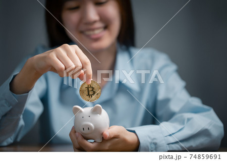 Woman is putting golden bitcoin into the piggy bank. Woman is putting golden bitcoin into the piggy bank. 74859691