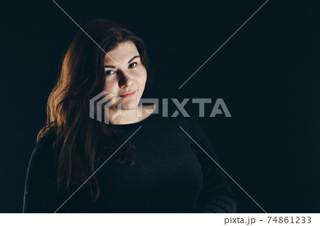 a beautiful girl with black hair posing on a black background in front of the camera 74861233