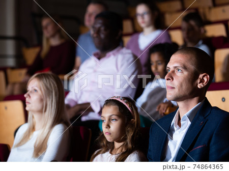 Father, mom and daughter are carefully watching spectacle or concert in theater auditorium 74864365