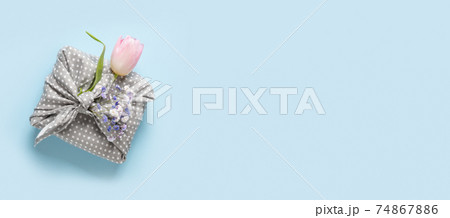 Spring sustainable gift wrapped in grey textile with tulip on blue. 74867886
