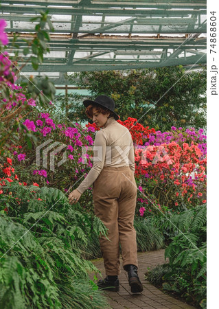 A beautiful plus size girl in a hat smiles among the green plants of greenhouse 74868604