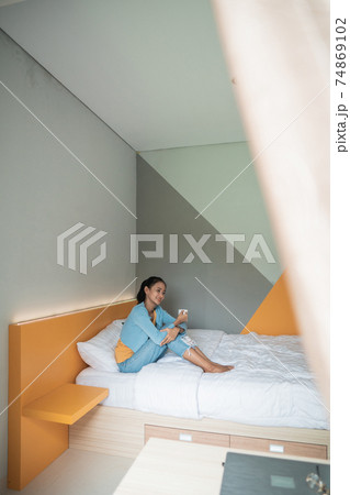 Attractive asian girl holding a cup with hot tea or coffee and looking at the window in her home and having a perfect cozy morning. Attractive asian girl holding a cup with hot tea or coffee and looking at the window in her home and having a perfect cozy morning. 74869102