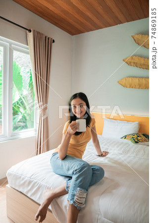 asian woman having coffee in cozy bedroom. Morning rituals. asian woman having coffee in cozy bedroom. Morning rituals. 74869185