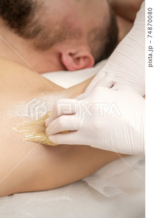 Beautician waxing young male armpit 74870080