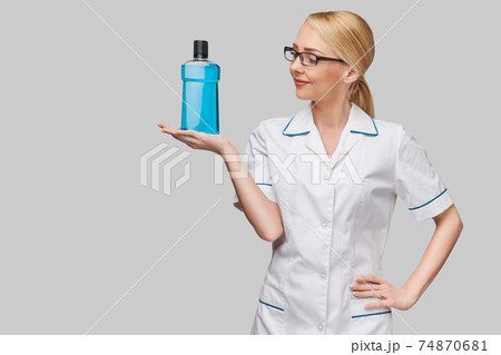 woman dentist doctor holding bottle of mouthwash standing over grey background woman dentist doctor holding bottle of mouthwash standing over grey background 74870681