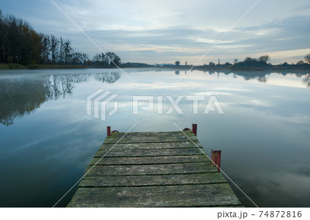 Wooden bridge towards a misty and calm lake Wooden bridge towards a misty and calm lake 74872816