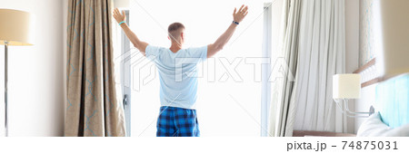 Young man stands with his back at open window in hotel room 74875031