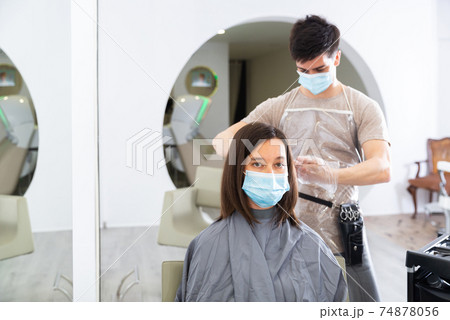 Woman client in mask during cuts hair at beauty salon 74878056