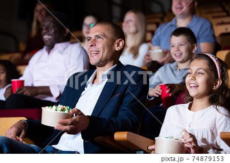 Cheerful family watching a movie and eating popcorn in cinema 74879153