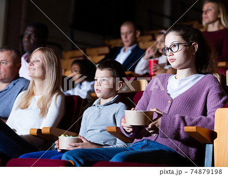 Teen girl with family watching film in movie theater Teen girl with family watching film in movie theater 74879198