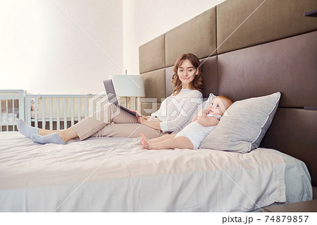 Baby and mother with a laptop working on a bed. Baby and mother with a laptop working on a bed. 74879857