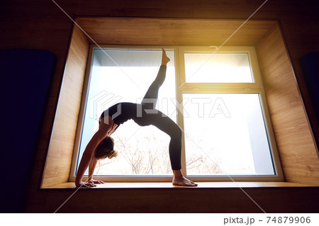 Woman doing yoga bridge on the background window. Exercising at Woman doing yoga bridge on the background window. Exercising at 74879906