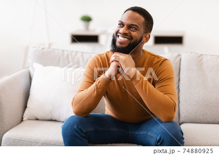 Happy African Guy Thinking Dreaming Sitting On Sofa At Home 74880925