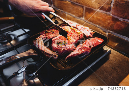 Hand turns steak with tongs during preparation on the grill pan with seasonings 74882718