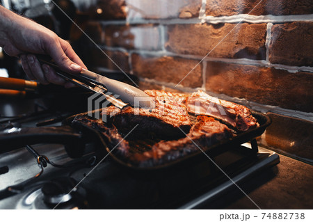 Hand turns steak with tongs during preparation on the grill pan with seasonings 74882738
