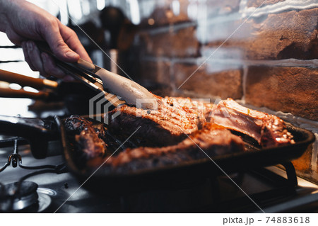 Hand turns steak with tongs during preparation on the grill pan with seasonings 74883618
