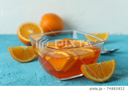 Bowl of orange jelly with orange slices on blue textured background Bowl of orange jelly with orange slices on blue textured background 74883852