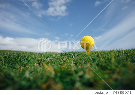 yellow golf ball on tee, green grass and blue sky background yellow golf ball on tee, green grass and blue sky background 74889071
