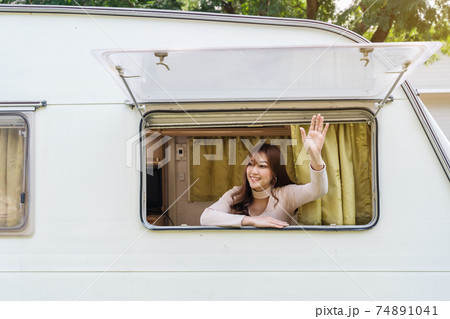happy woman raising her hand at window of a camper RV van motorhome happy woman raising her hand at window of a camper RV van motorhome 74891041