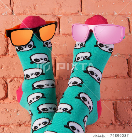 two legs in turquoise socks with a picture of panda faces, stick up, leaning on a brick wall, on the legs are two colored sunglasses, concept two legs in turquoise socks with a picture of panda faces, stick up, leaning on a brick wall, on the legs are two colored sunglasses, concept 74896087