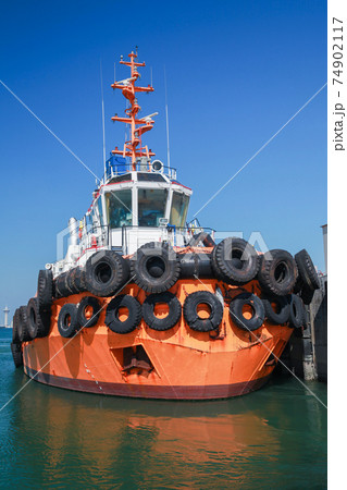 Tug boat with  bright orange hull is moored in a port 74902117