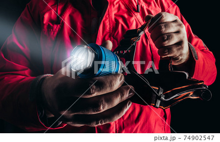 Close-up product photo of hiker man in red travel camping jacket holding shining head flashlight. 74902547