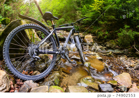 Photo of mountain bicycle standing in forest river landscape background. Photo of mountain bicycle standing in forest river landscape background. 74902553