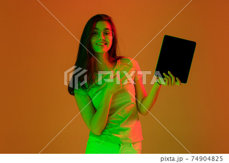 Beautiful girl with digital tablet isolated on studio background in neon light. 74904825