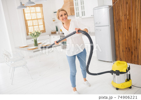 Cheerful woman with vacuum cleaner in kitchen Cheerful woman with vacuum cleaner in kitchen 74906221