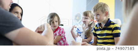 Adults and children are sitting around table on which playing cards are located boy looks thoughtfully at adults Adults and children are sitting around table on which playing cards are located boy looks thoughtfully at adults 74907585
