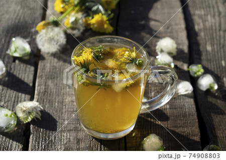 Medicinal Tea from dandelion in glass cup and flower dandelion on wooden rustic table with ice Medicinal Tea from dandelion in glass cup and flower dandelion on wooden rustic table with ice 74908803