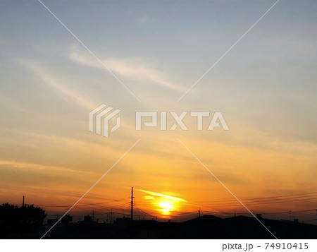 夕暮れのグラデーションの空と滲む夕日が見える街並みのシルエットの風景の写真素材