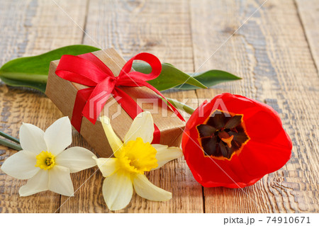 Flowers of daffodils and tulip with gift box on wooden boards 74910671