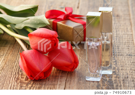 Bottles of perfume and gift box on wooden boards with flowers 74910673