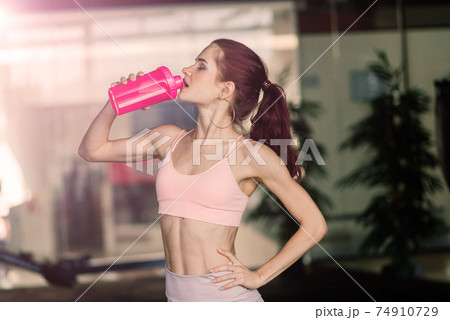 Young female at the gym trainer holding a bottle of water Young female at the gym trainer holding a bottle of water 74910729