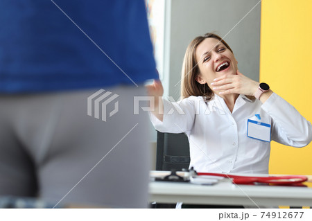 Woman doctor laughing at male patient in shorts in clinic Woman doctor laughing at male patient in shorts in clinic 74912677